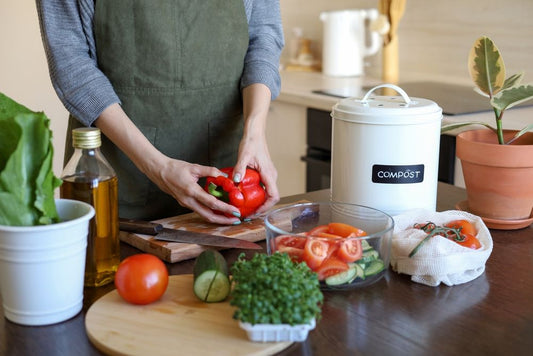 A person chopping vegetable next to a compost bin