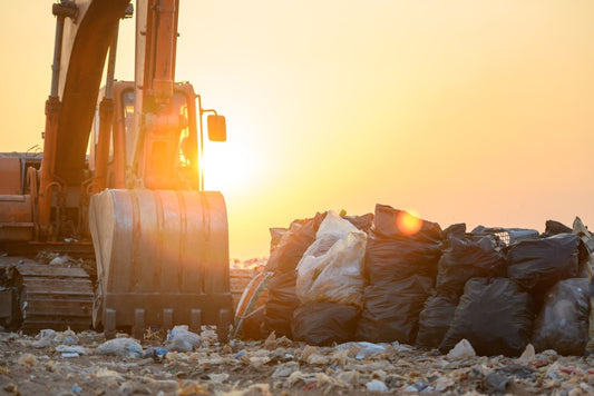 A bulldozer beside several bags of trash in a landfill