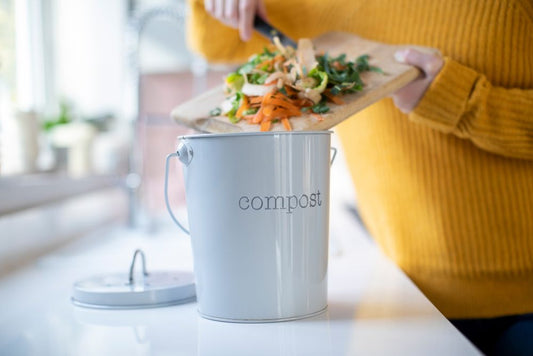 A woman scraping veggie peels into a gray compost bin