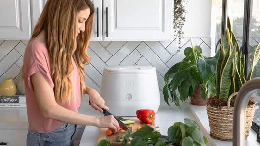 Lomi composter in a kitchen next to a woman cutting vegetables