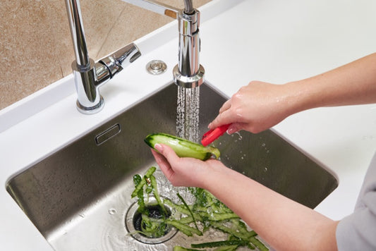 Someone peeling a cucumber over their sink