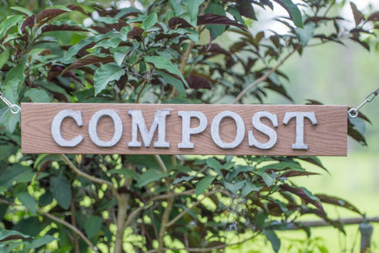 A sign on a tree that has an arrow and says compost